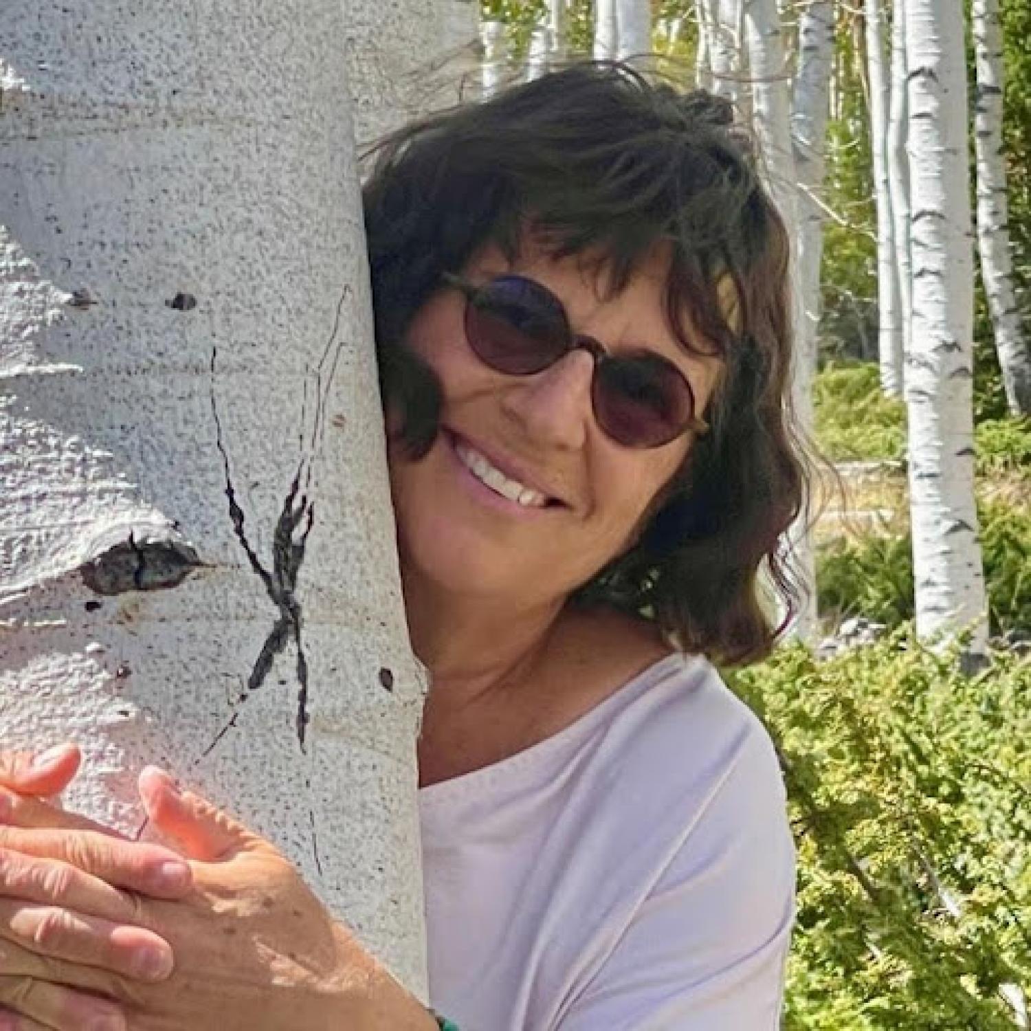 Rita Vali standing hugging an aspen tree