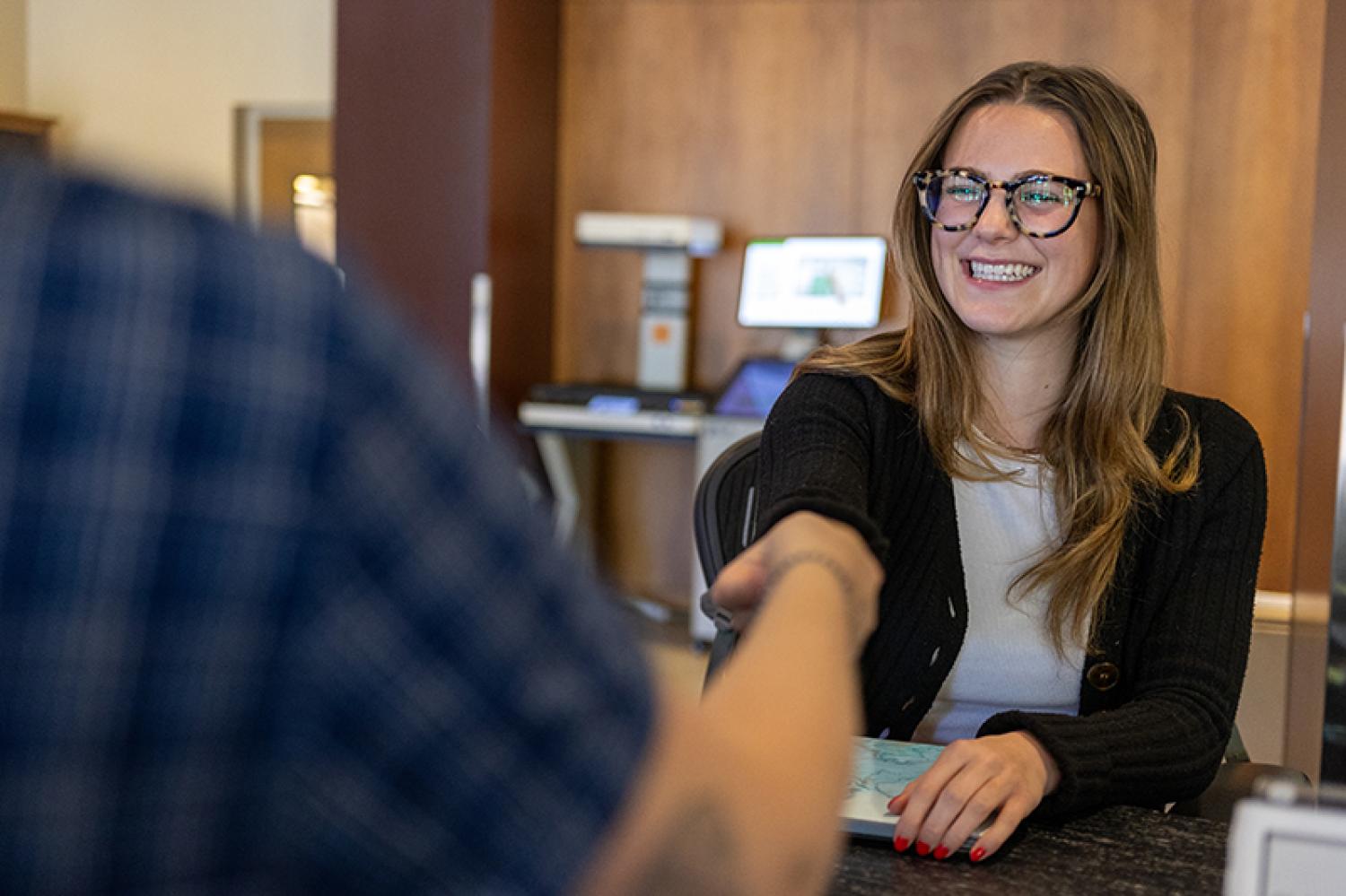 Someone checks out a book from a smiling Libraries service desk worker.