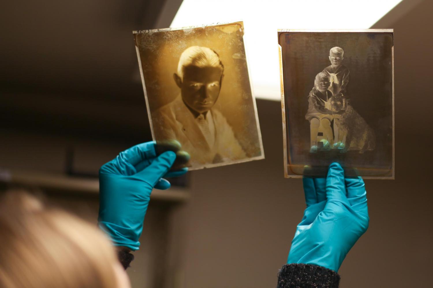 With blue gloves, the photo archivist holds up two old negatives to a light.