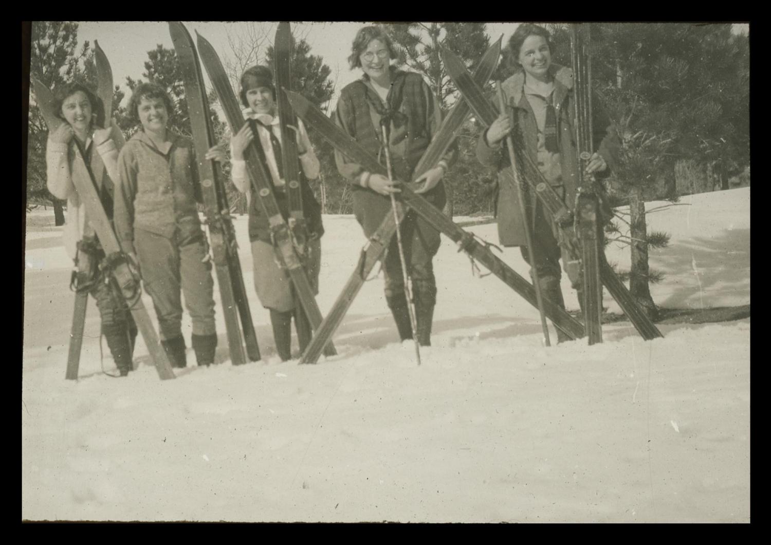 Black and white image of five women with ski gear in the snow, year unknown.